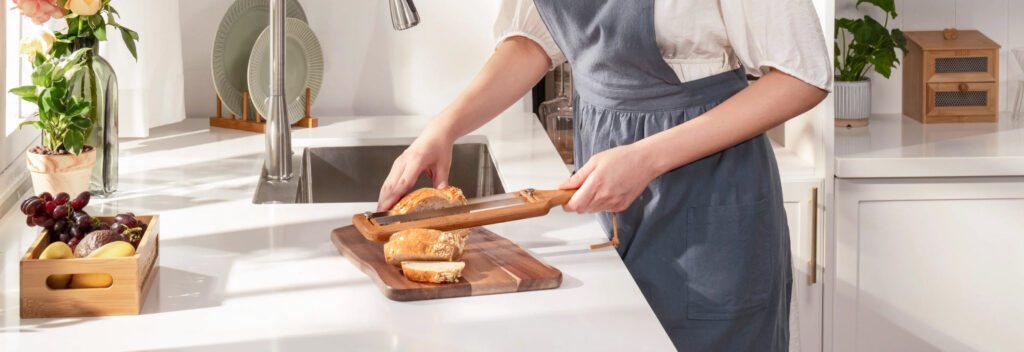 How to Slice Homemade Bread Evenly Without Crushing It Person slicing a small loaf with a bamboo bread slicer on a kitchen cutting board.